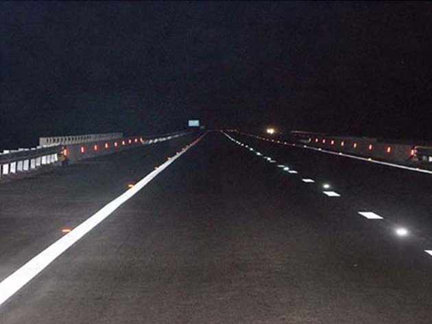 A road at night with freshly painted white lines and reflective raised markers catching the light