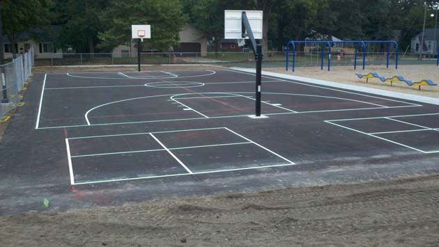 Two basketball half courts with white lines and hoops beside a playground