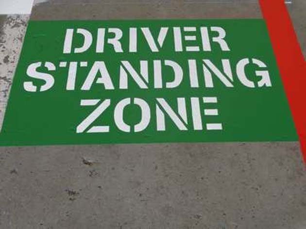 The words DRIVER STANDING ZONE stencilled in white on a green painted panel on a concrete floor