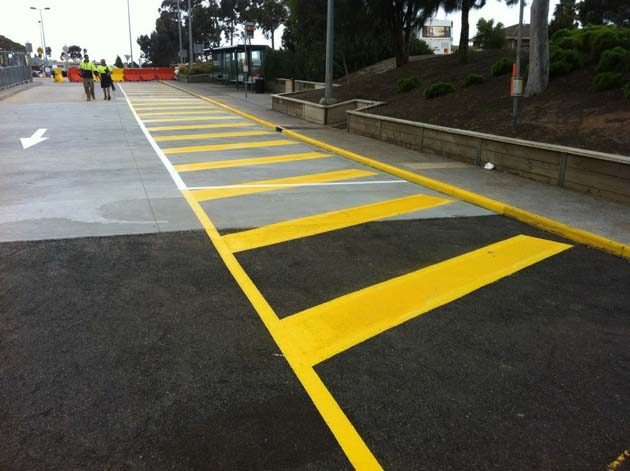 Yellow hatched crossing bars on asphalt beside a yellow painted kerb and a white line