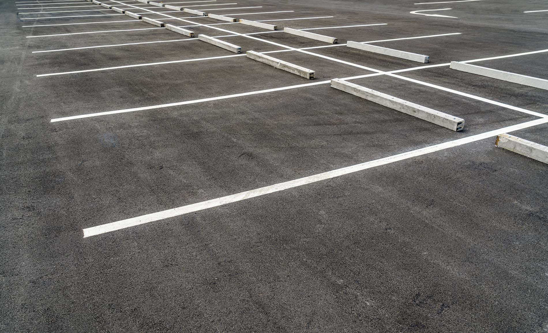 Freshly painted white parking bay lines and concrete wheel stops across a wide asphalt car park