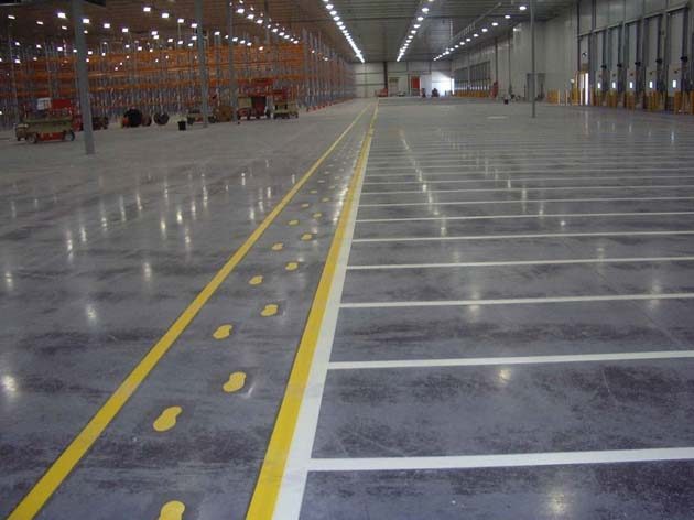 A polished warehouse floor with a yellow pedestrian walkway marked with footprints and white bay lines beside it